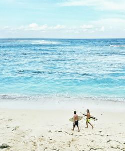 Rear view of men walking on beach against sky