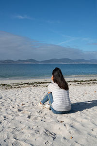 Woman sit and relaxing on the white sand of oia beach in galicia, spain