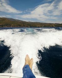 Low section of man relaxing by sea against sky