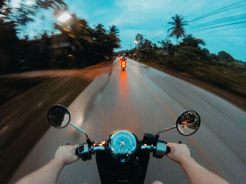 Cropped hands riding motorcycle on road at dusk