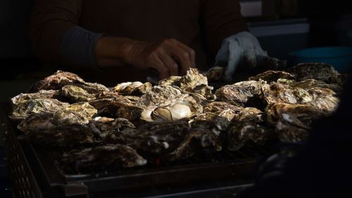 Midsection of person preparing grilled oysters 