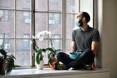 Full length of man sitting by window at home