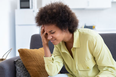 Young woman looking away while sitting on sofa at home