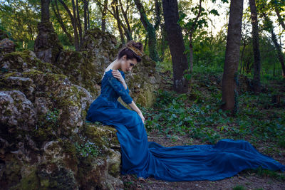 Side view of young woman wearing blue dress in forest