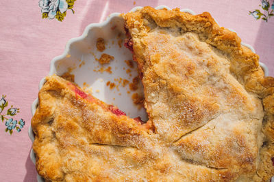 Rhubarb pie with missing slice, pink tablecloth with blue roses,