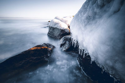 Water flowing through rocks by sea against sky