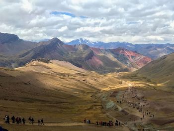 Group of people on mountain range against cloudy sky