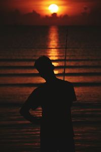 Silhouette man standing by sea against sky during sunset