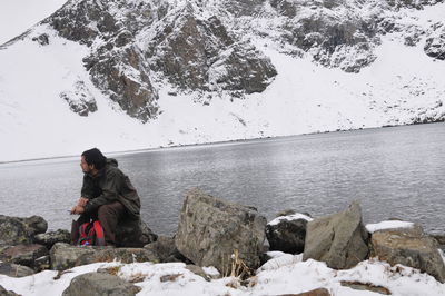 Woman sitting on rock by snow covered mountain against sky