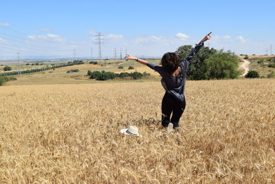 Rear view of excited woman running on field with arms outstretched against sky