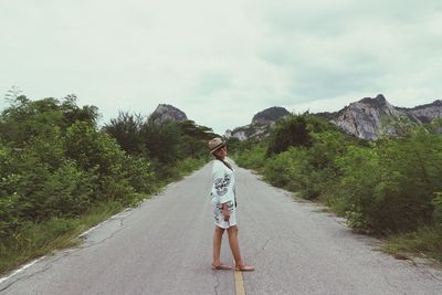 Rear view of woman standing on road amidst trees against sky