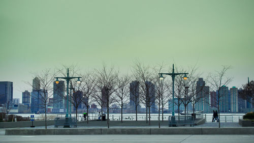 Bare trees in city against clear sky