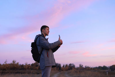 Young man standing on land against sky during sunset