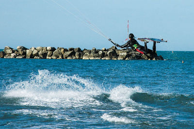 Person parasailing in sea against clear blue sky