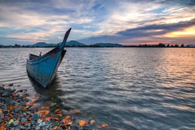 Boat moored in sea against cloudy sky during sunset