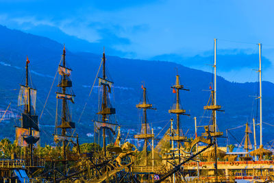 Old ships moored at harbor by mountains against sky at dusk