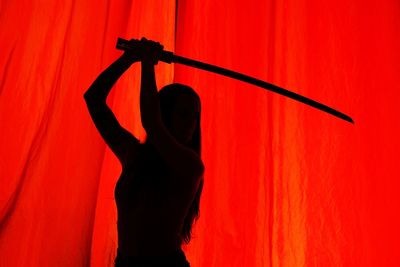 Shadow of woman with sword seen through red curtain