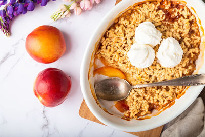 Fresh homemade nectarine crumble with vanilla ice cream in ceramic form on white marble background