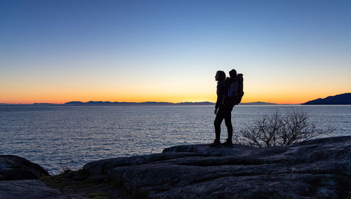 Rear view of woman standing at beach against clear sky during sunset