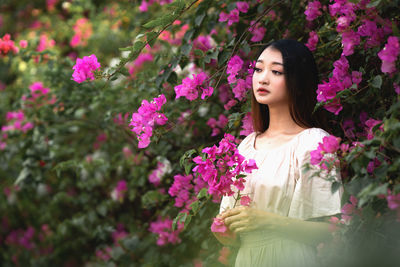 Beautiful woman standing by pink flowering plants