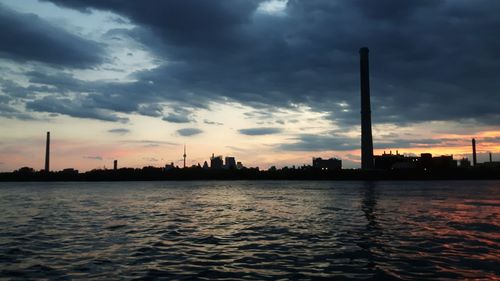 River by cityscape against sky during sunset