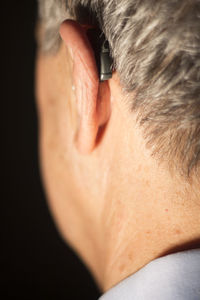 Close-up of man wearing hearing aid against black background