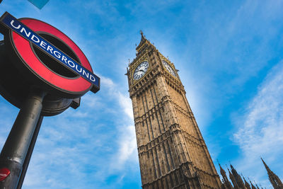 Low angle view of signboard and clock tower against blue sky