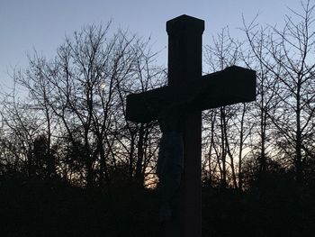 Low angle view of cross on silhouette bare tree against sky