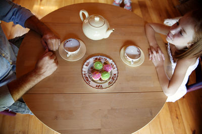 Overhead view of father and daughter sitting at table with cupcakes and tea