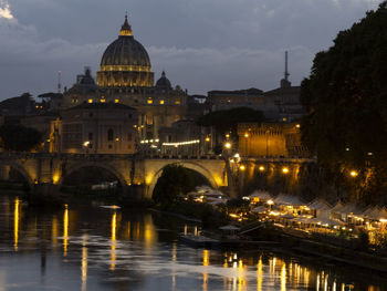 Illuminated bridge over river against buildings in city