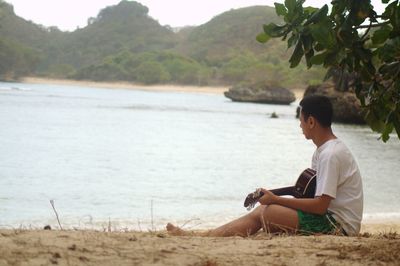 Side view of man sitting on beach