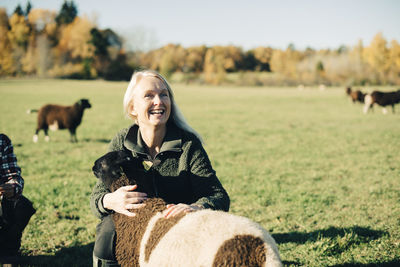 Smiling mature female farmer embracing sheep on field