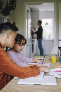 Gay man assisting daughter doing homework while sitting at dining table in home