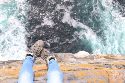 Low section of person sitting on cliff by sea