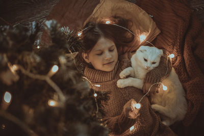 Cozy girl and domestic cat are under the christmas tree, dark golden style. 