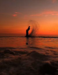 Side view of silhouette man splashing water in sea against sky during sunset