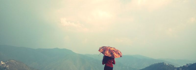 Rear view of woman standing on mountain against sky