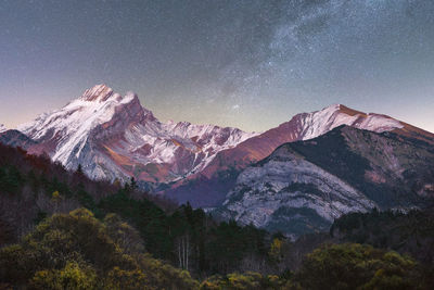 Scenic view of dark mounts with snow and rough peaks under starry sky at dusk