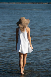 Young unrecognized woman wearing a white summer dress and hat walking in the beach. 