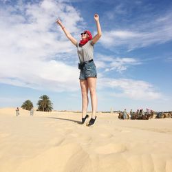 Woman with arms raised on beach against sky