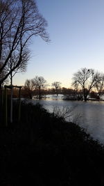Silhouette bare trees by lake against clear sky