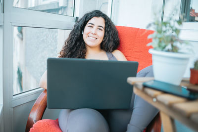 Smiling young woman using laptop sitting on sofa