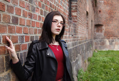 Portrait of a young woman standing against brick wall