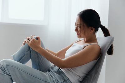 Woman holding knee sitting on chair at home