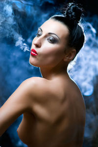 Side view of shirtless woman emitting smoke from mouth at night