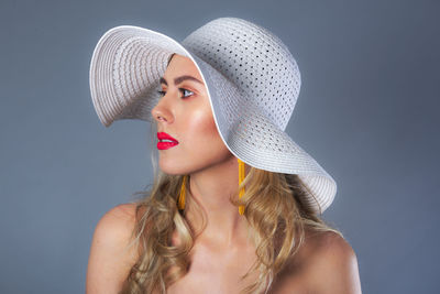 Portrait of young woman wearing hat against gray background