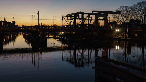 Silhouette bridge over river against sky during sunset