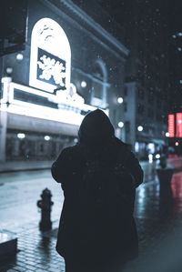 Man standing on wet street in city during winter at night