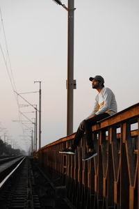 Side view of man standing on railroad tracks against clear sky