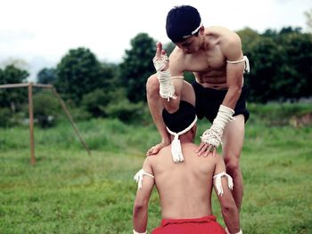 Shirtless male fighters practicing on grass against sky